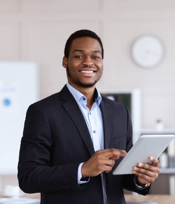 Smiling black entrepreneur young man holding digital tablet, using modern technologies in business, office interior, copy space. Cheerful african american businessman using app for business